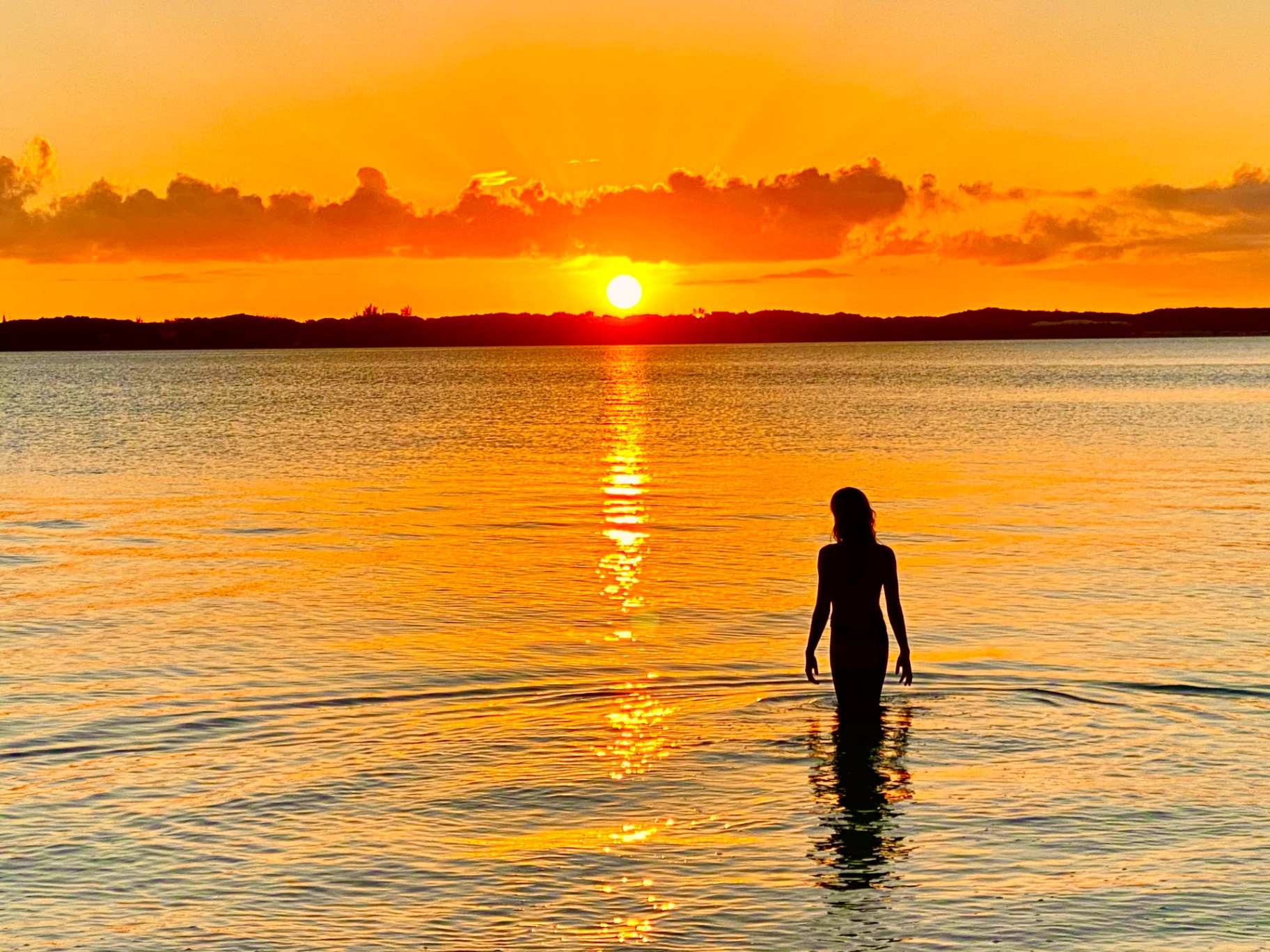 Silhouette walking into a golden Bahamian sunset over still water